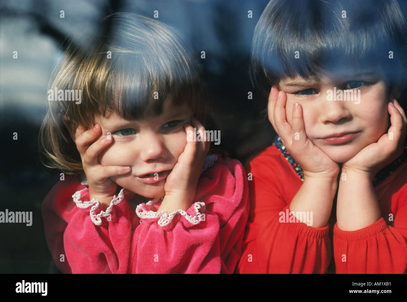 Two young girls looking out the window in dismay Stock Photo