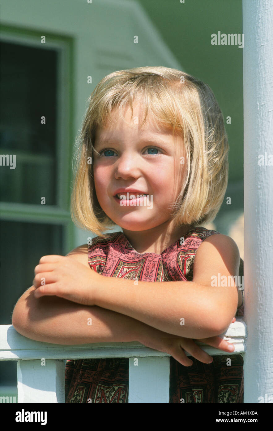 Young blonde girl leaning on porch railing Stock Photo