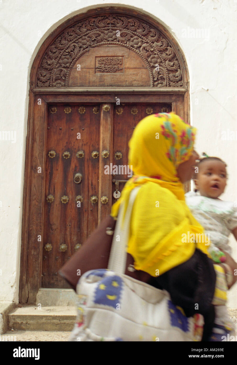 A Zanzibari woman and child walking past a beautiful wooden carved door Stone Town Zanzibar Tanzania Stock Photo