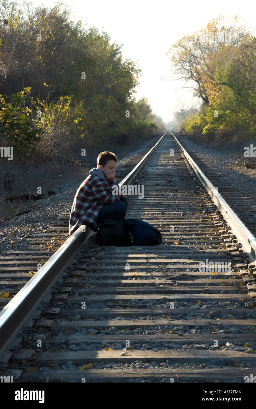 A thirteen-year-old caucasian boy runaway resting sitting on a rail of a railroad track. Stock Photo