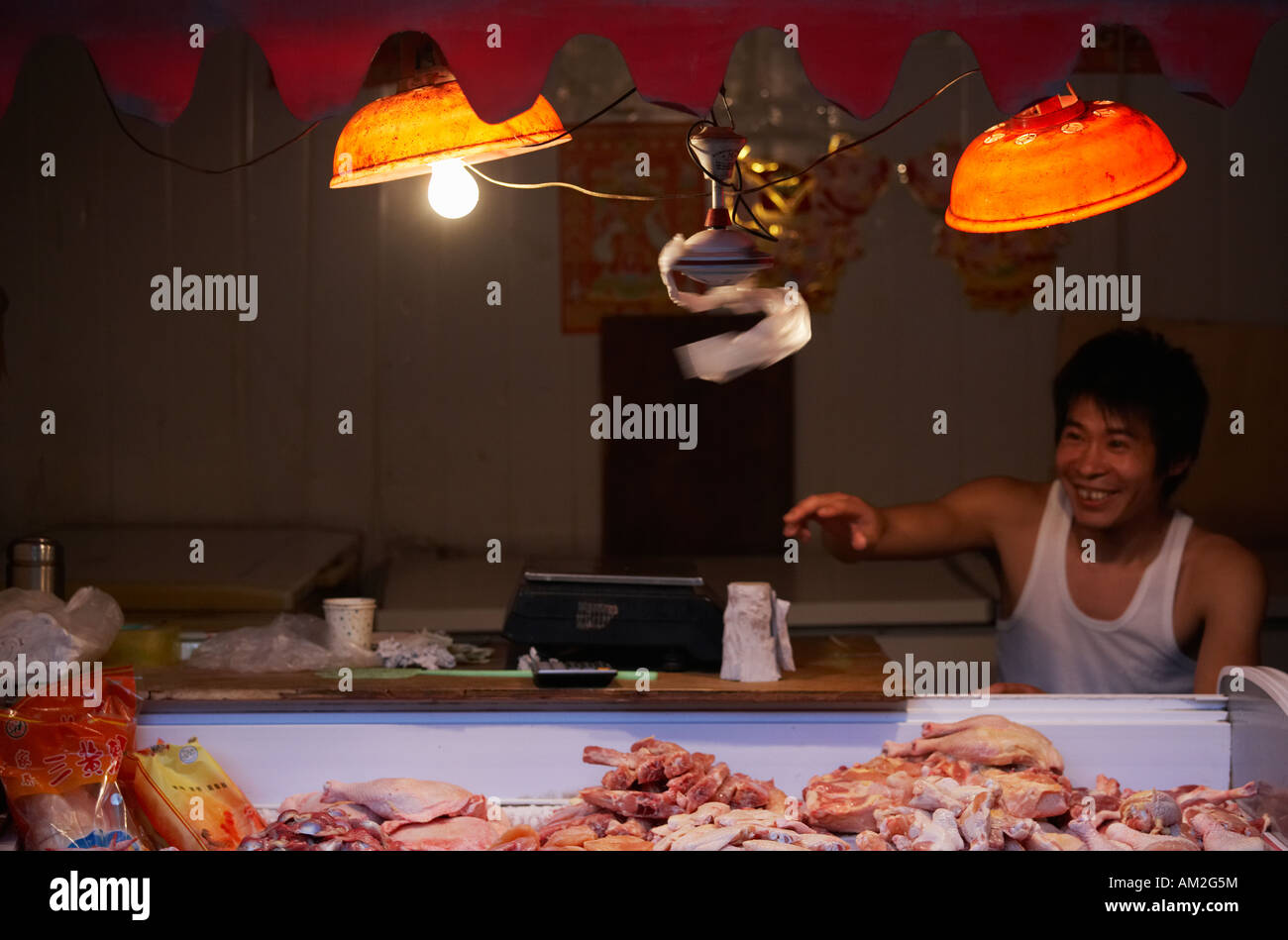 Smiling man behind illuminated meat stall in hutong Beijing China Stock Photo