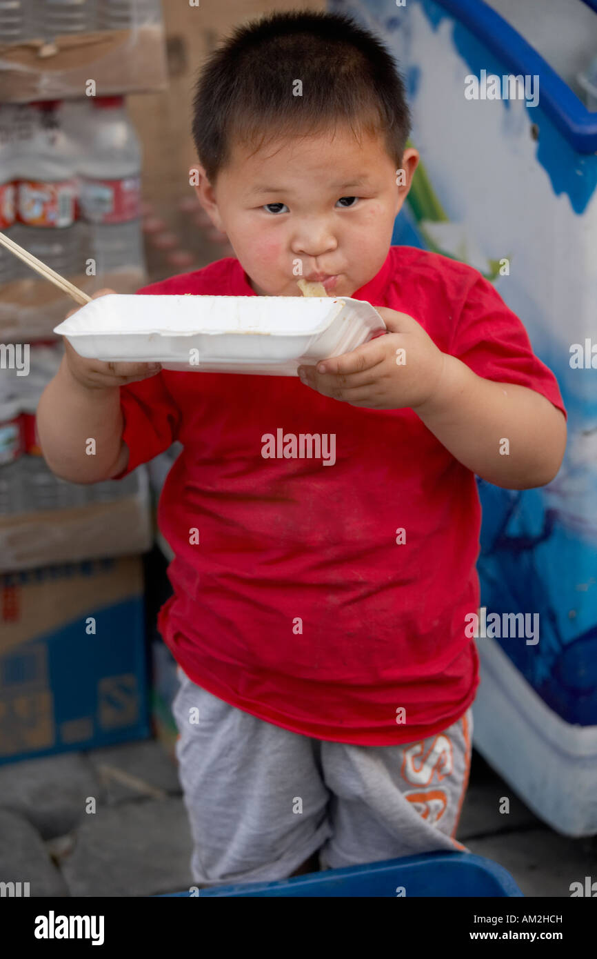 Chinese toddler standing and eating in hutong Beijing China Stock Photo