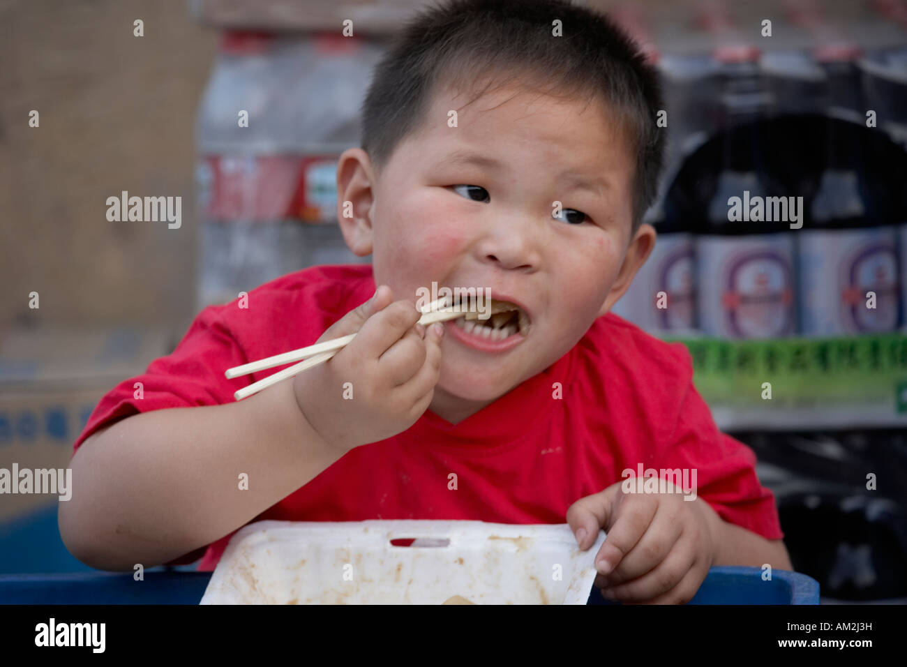 Chinese toddler eating with chopsticks in hutong Beijing China Stock Photo