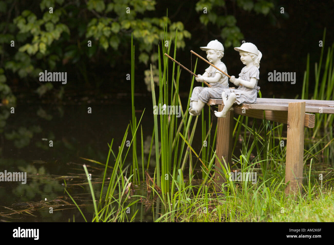 Ornamental stone statues of kids sitting on pier fishing Stock Photo