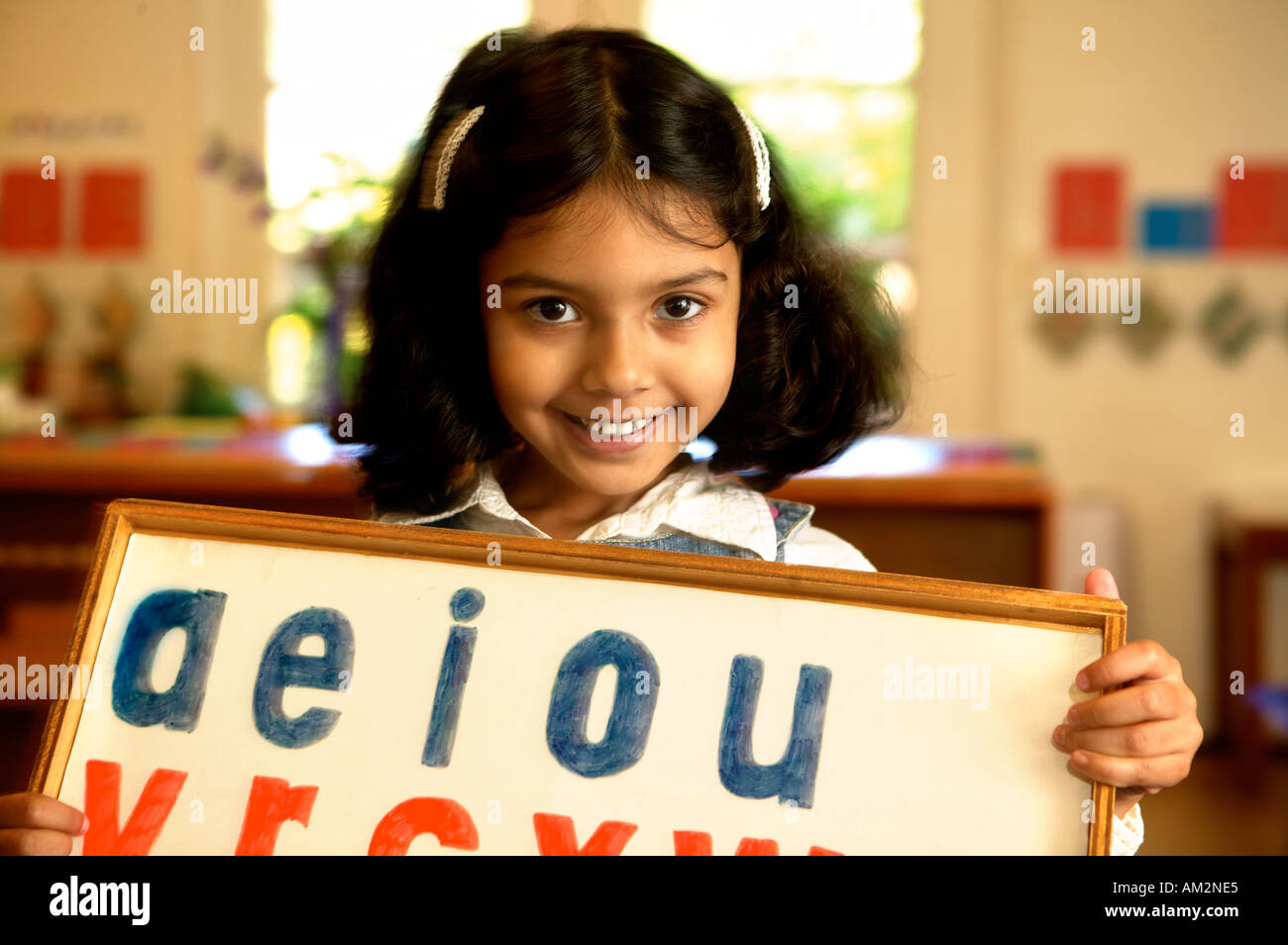 A preschooler holds up a board of vowels in her preschool classroom Stock Photo
