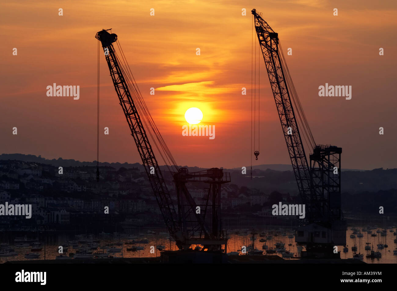 Cranes at Falmouth docks silhouetted at sunset with yachts and boats moored behind. Falmouth, Cornwall, UK Stock Photo