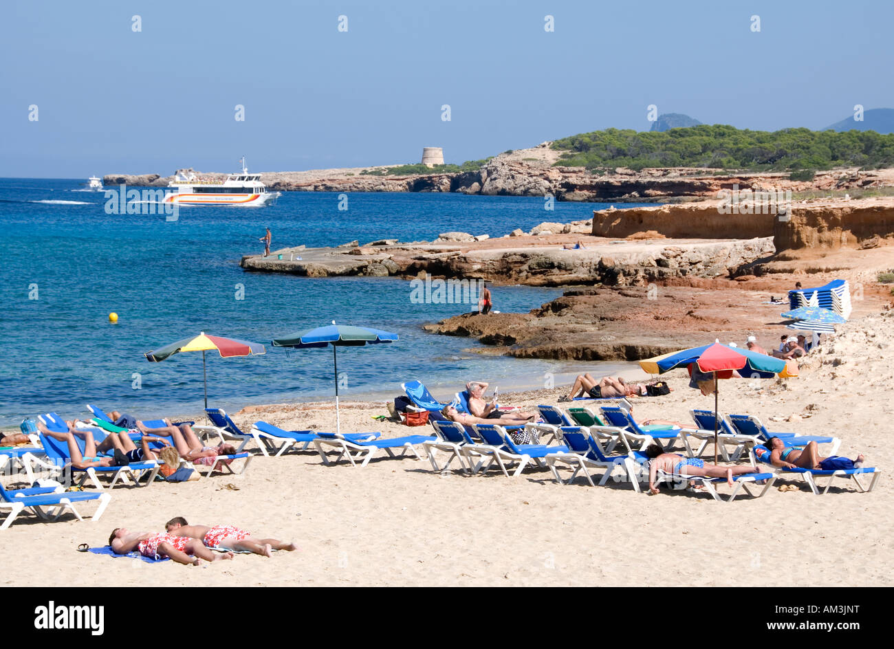 Tourists on the beach at Platges de Comte, Ibiza with a ferry in the distance Stock Photo