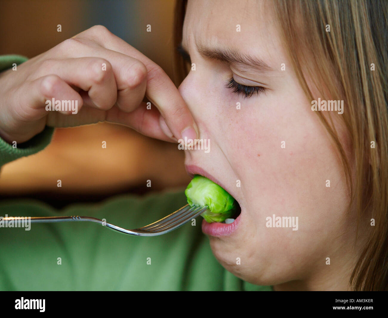 Girl 11 years old eating Brussels sprouts while pinching nose smelly Stock Photo