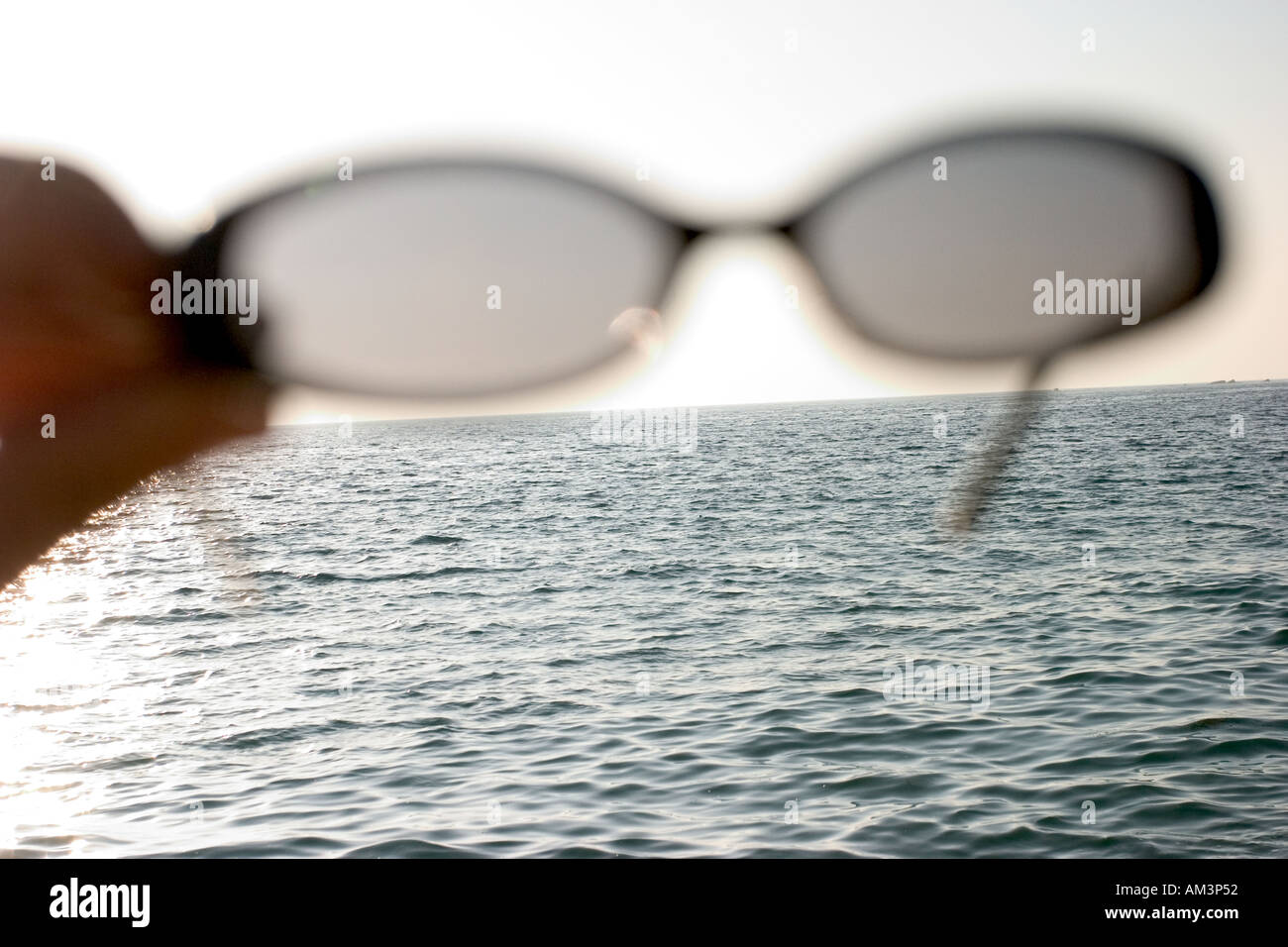 vacation Concept image of single alone sunglasse pair holding by male man hand with ocean sea horizon in the back Stock Photo