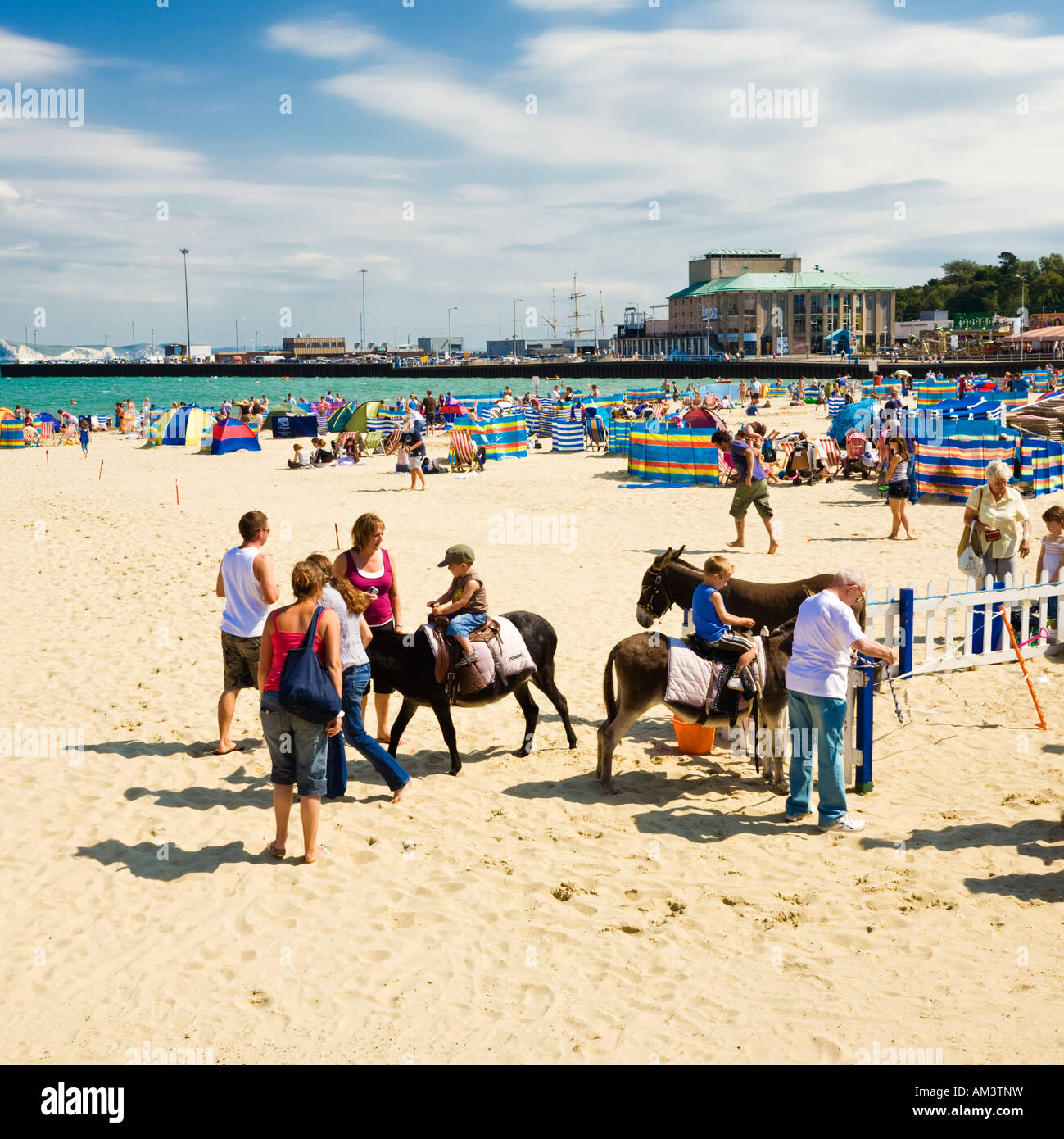 Children on donkeys at British seaside beach in summer at Weymouth beach in Dorset, England, UK Stock Photo
