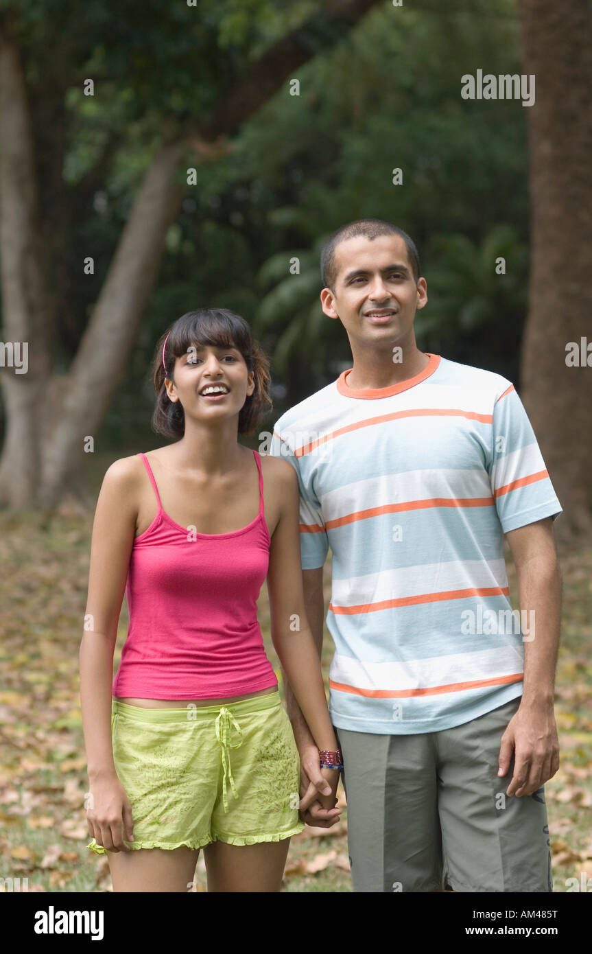Young couple standing in a park and smiling Stock Photo - Alamy