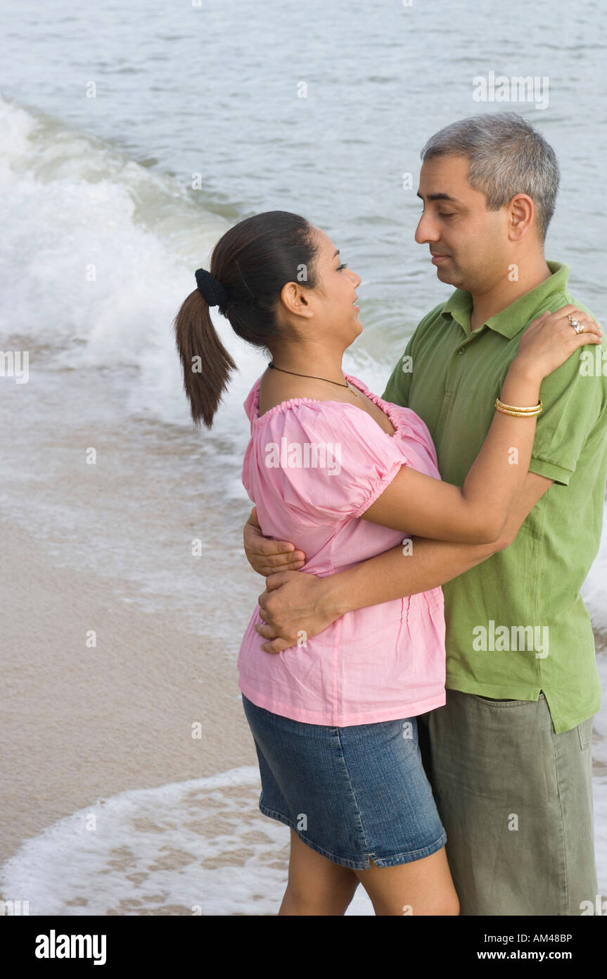 Side profile of a mid adult couple embracing each other on the beach ...
