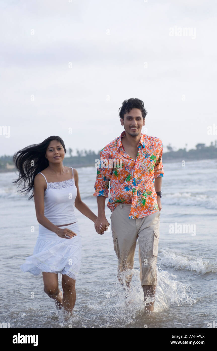 Portrait of a young couple running with holding hands on the beach ...