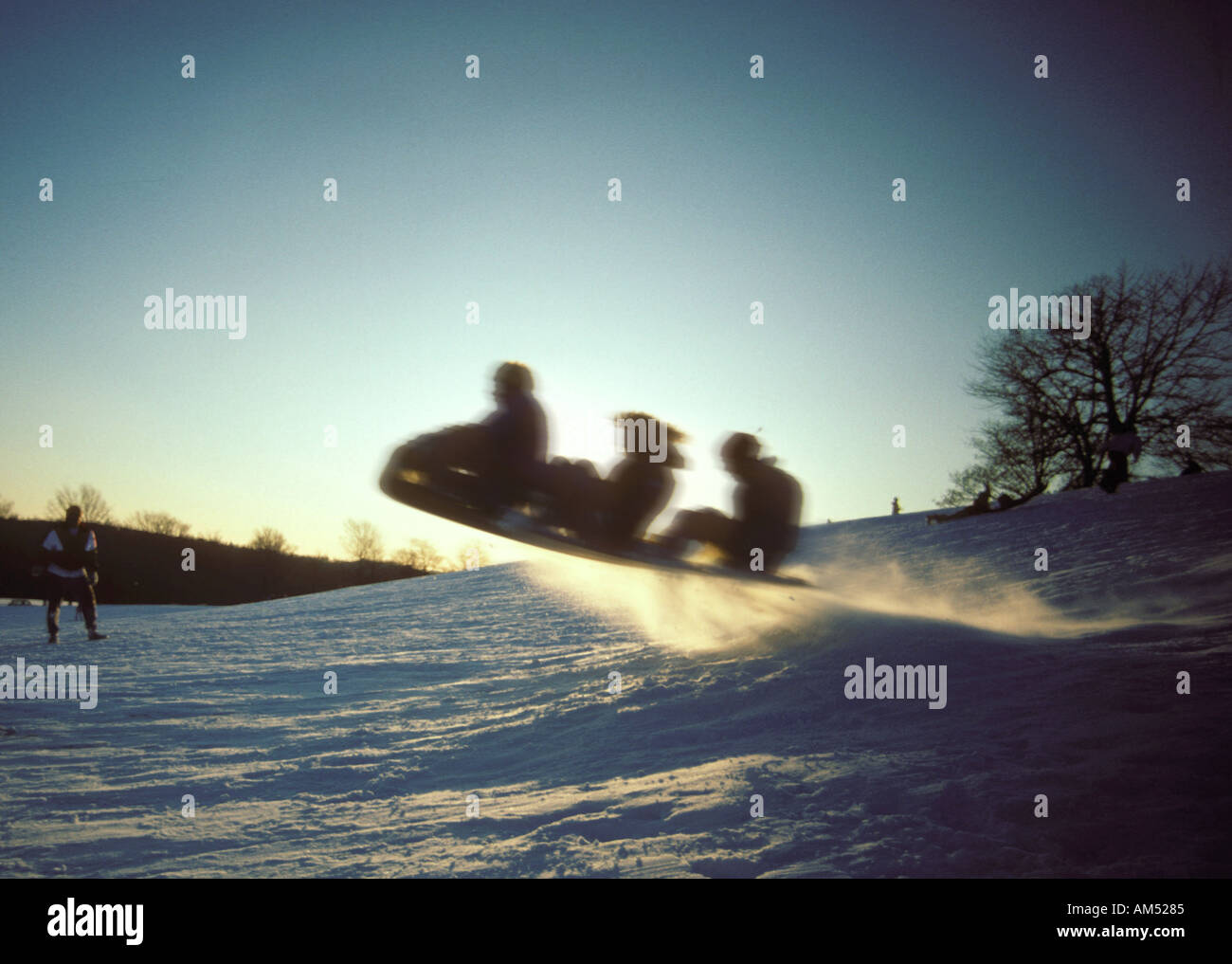 three people take a toboggan down a hill and over a jump Stock Photo