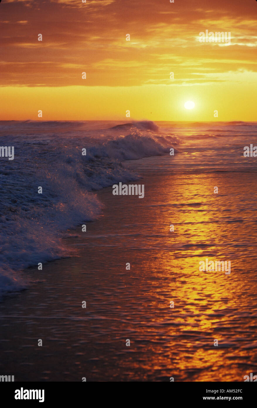 waves break on an ocean beach during a colorful sunset Stock Photo