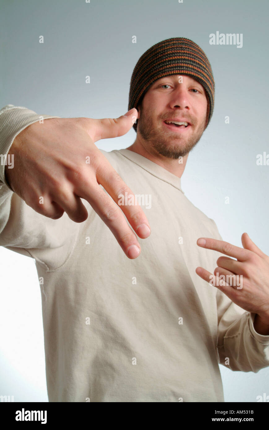 a young tough in a ski hat and T-shirt makes a threatening gun gesture with his fingers Stock Photo