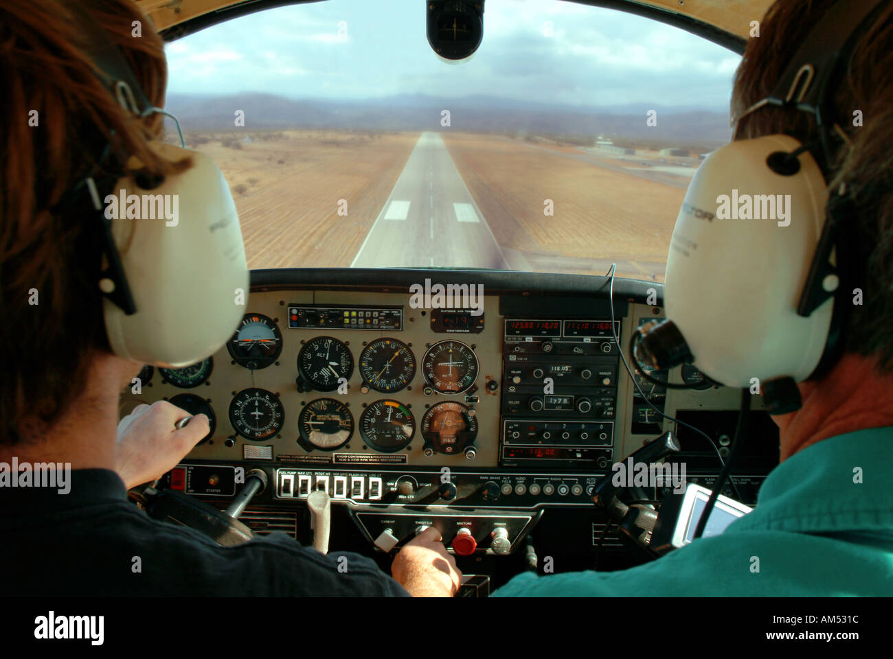 2 pilots landing a a small single engine airplane. The runway is seen