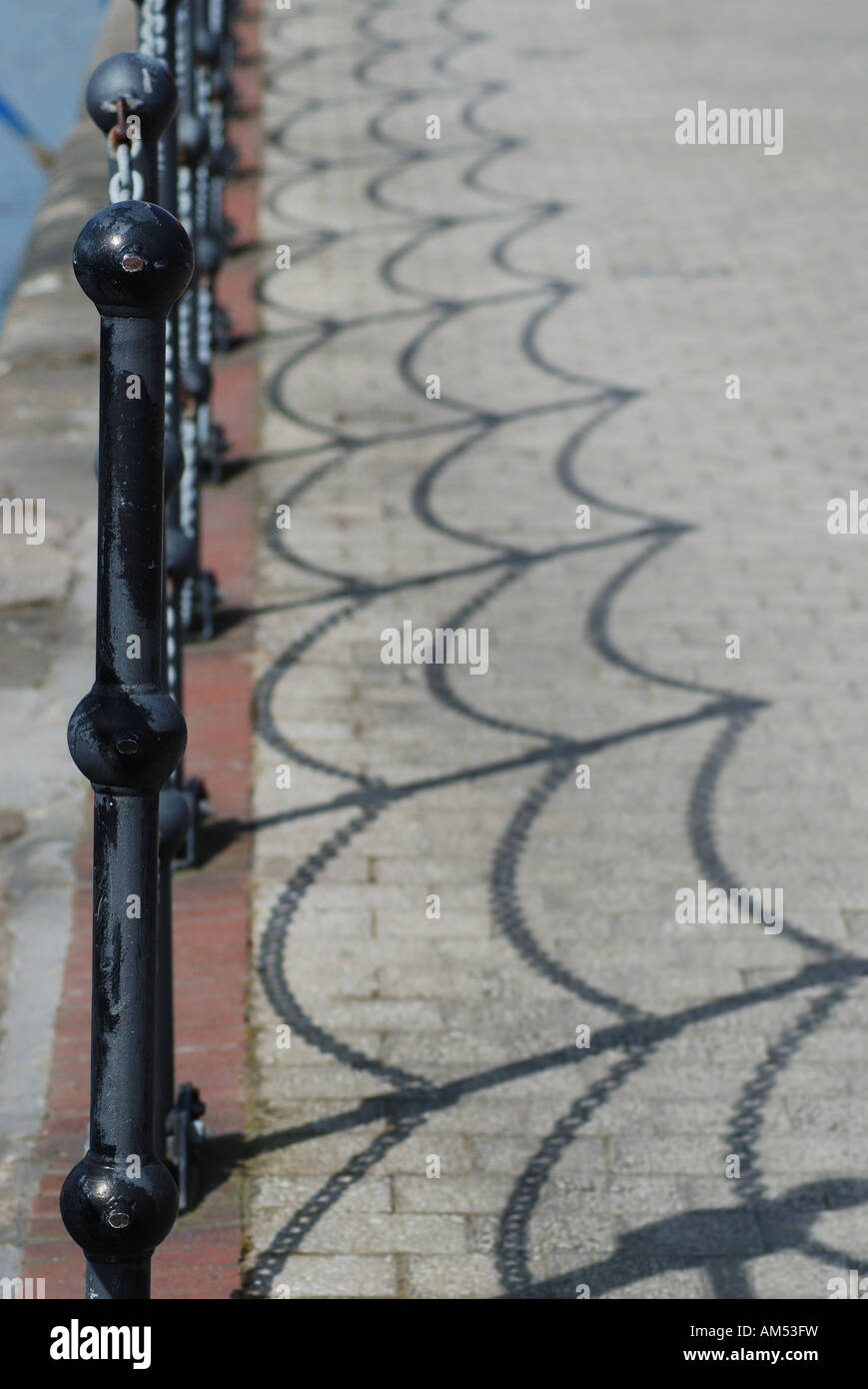 Chains on wrought iron posts sun casts shadow on paving stones Stock Photo