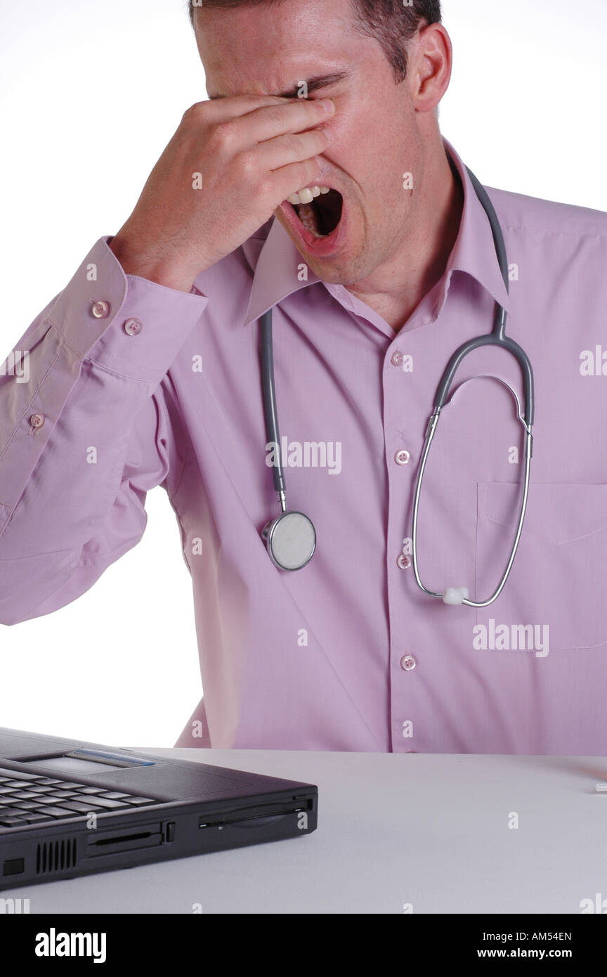 A young male doctor at his desk rubbing his eyes with fatigue from working long hours Stock Photo