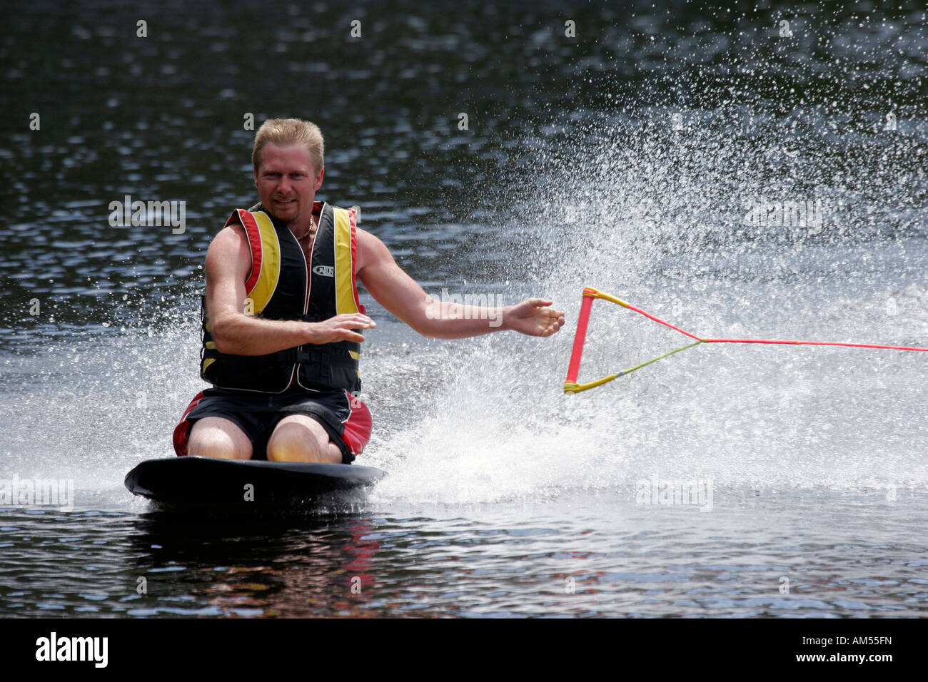 A young man enjoying his vacation on a lake riding a knee board behind a  boat just releasing the rope Stock Photo - Alamy