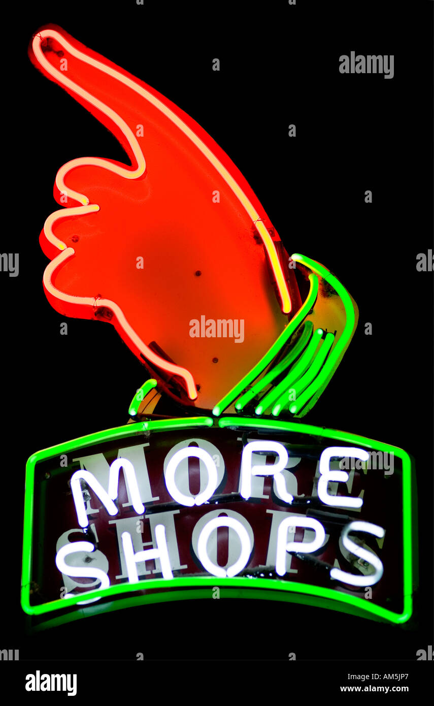 Neon sign More shops with a hand pointing to the left and upwards. Black background Stock Photo