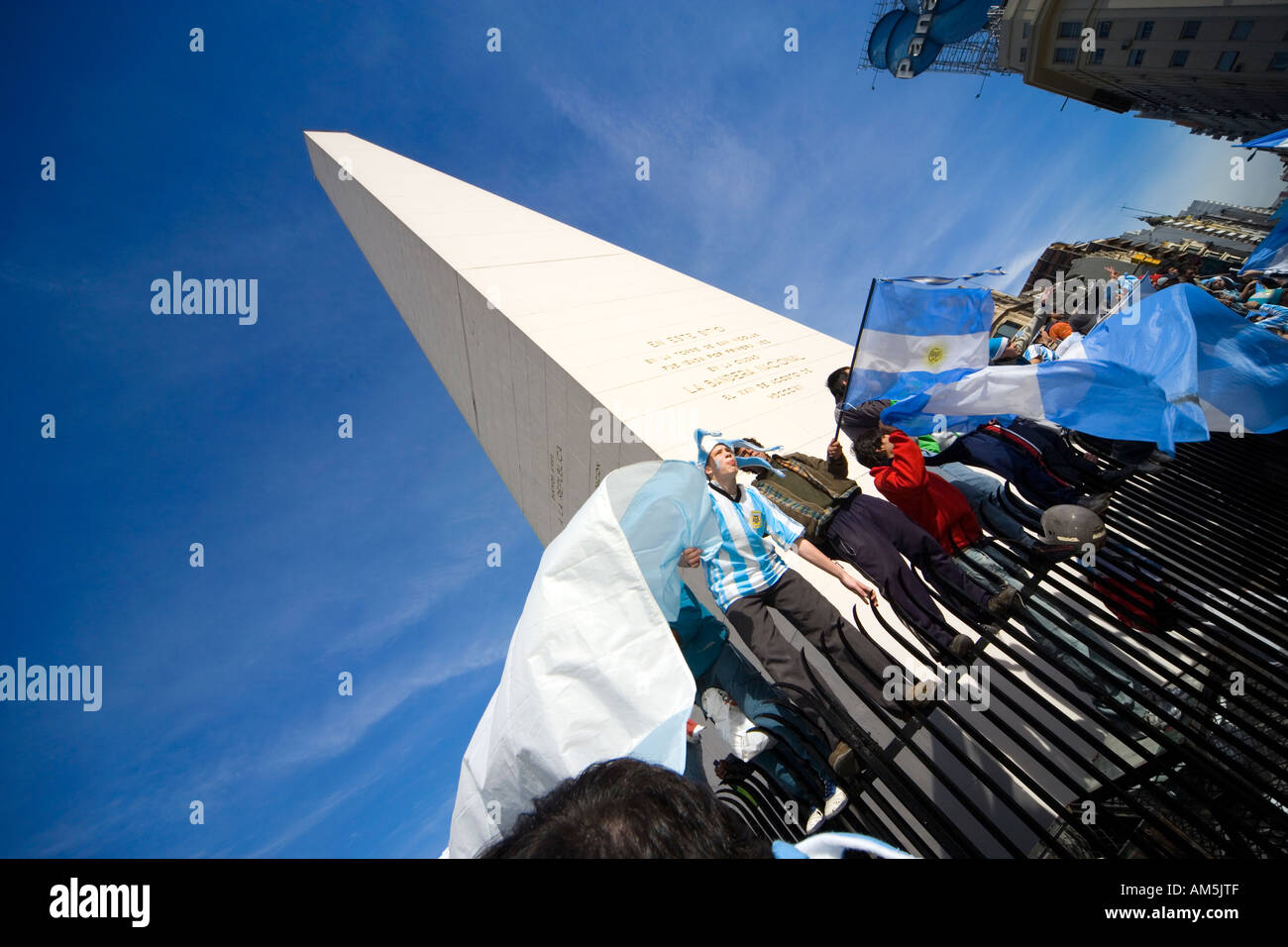Football soccer fans sing and cheer balancing dangerously on a sharp fence around the Obelisk waving Argentinian flags. Stock Photo