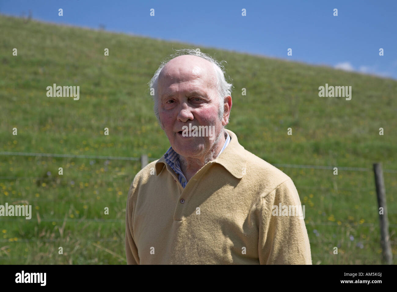 Portrait of elderly man in the countryside in front of green grassy hill of Wiltshire chalk downland on summer day with blue sky Stock Photo