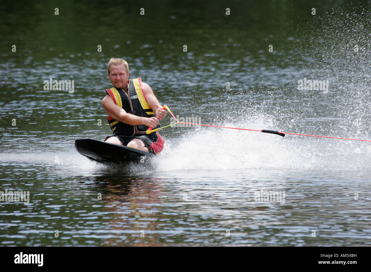 A young man enjoying his vacation on a lake riding a knee board behind