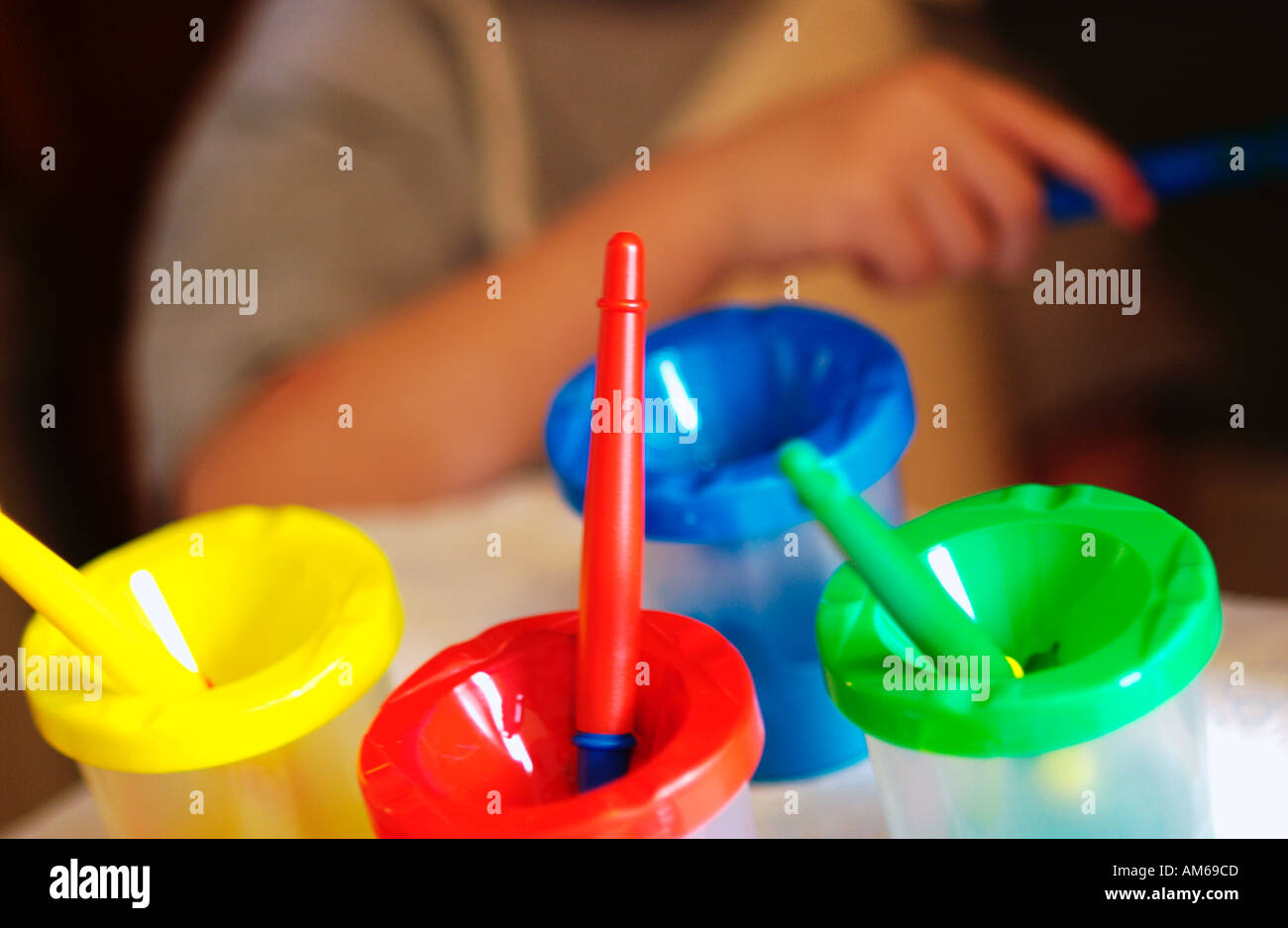 Yellow Blue Green and Red paints with kid painting in background Stock Photo