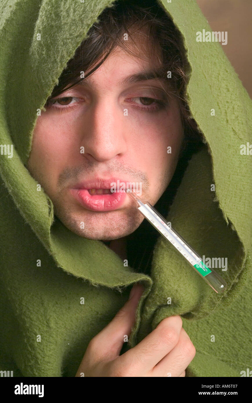 Sick male with blanket wrapped around his head and a thermometer in his