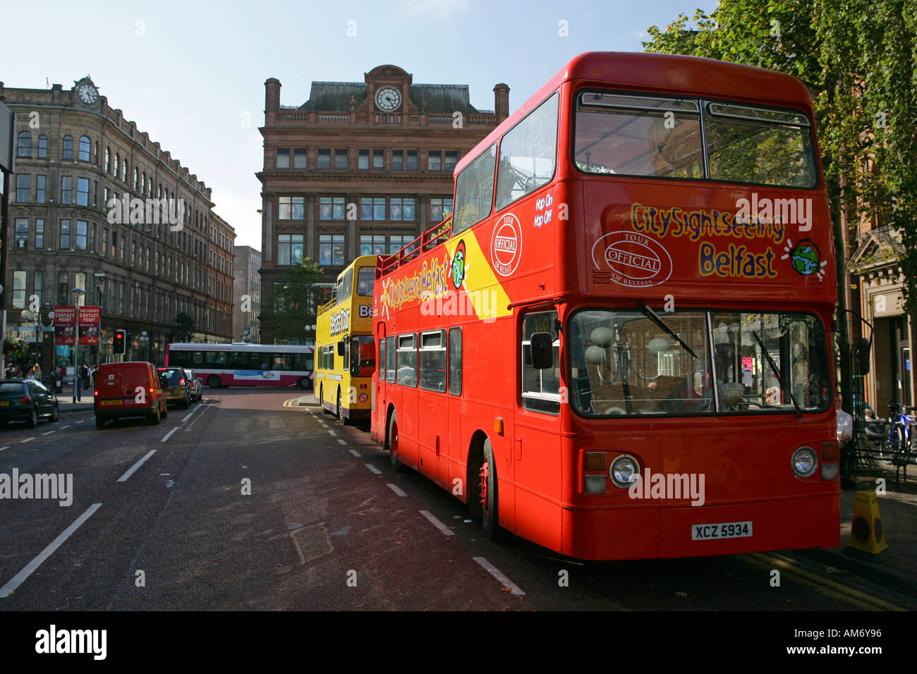 Open top bright red and vivid yellow tour buses wait for tourists in central Belfast city centre, Northern Ireland UK GB Stock Photo