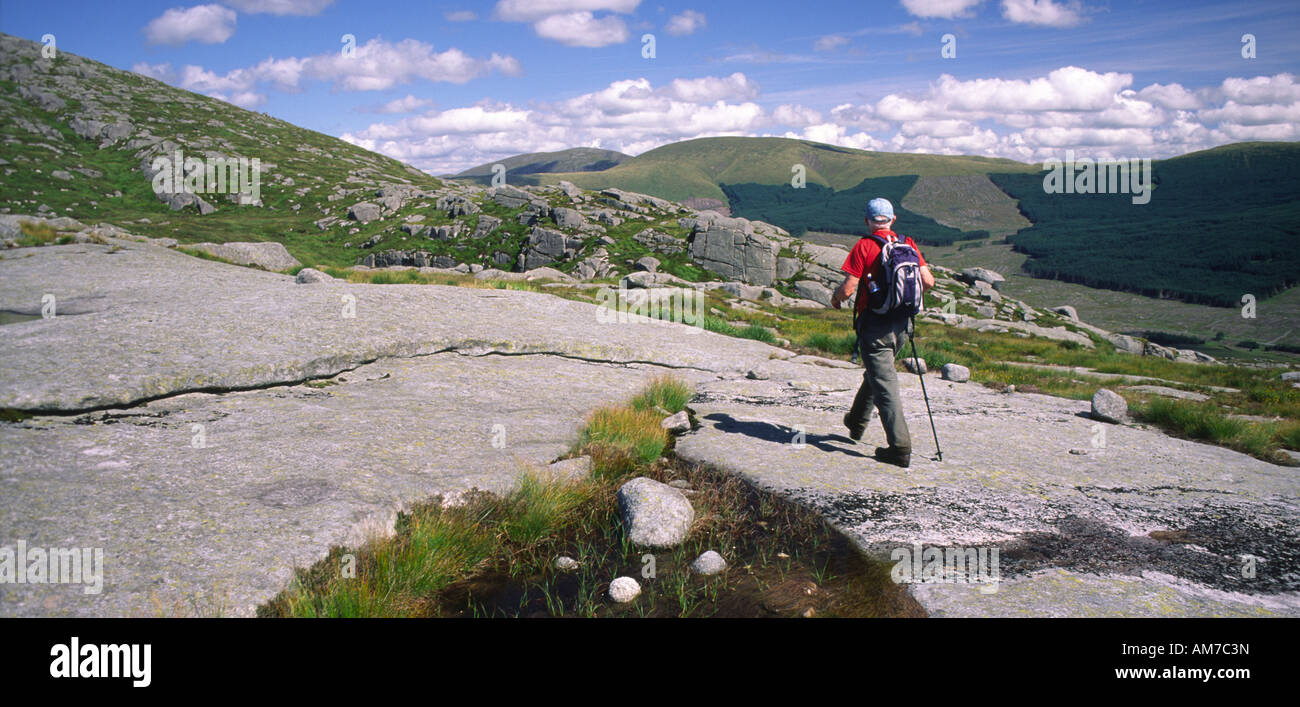 Hill walking in the Galloway Forest Park hill walker walking on granite slad up to Snibe Hill Galloway Scotland UK Stock Photo