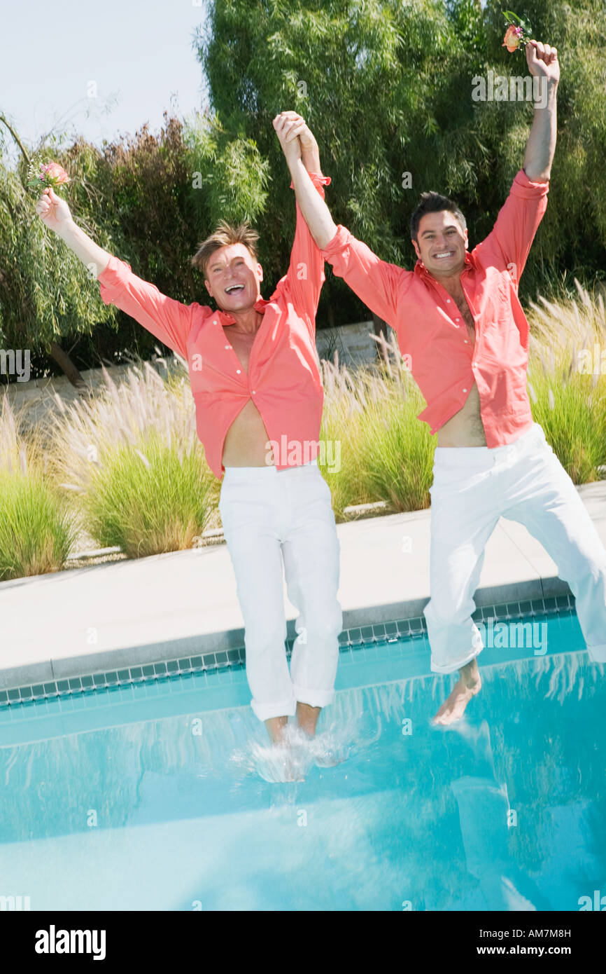 Fully clothed gay couple jumping into swimming pool Stock Photo