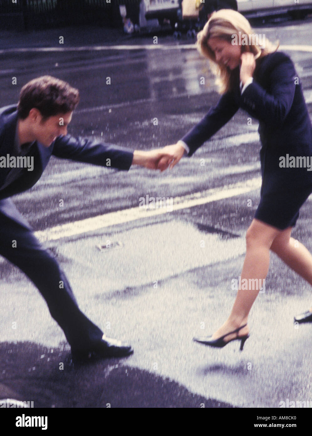 Young man holding woman's hand on wet road Stock Photo