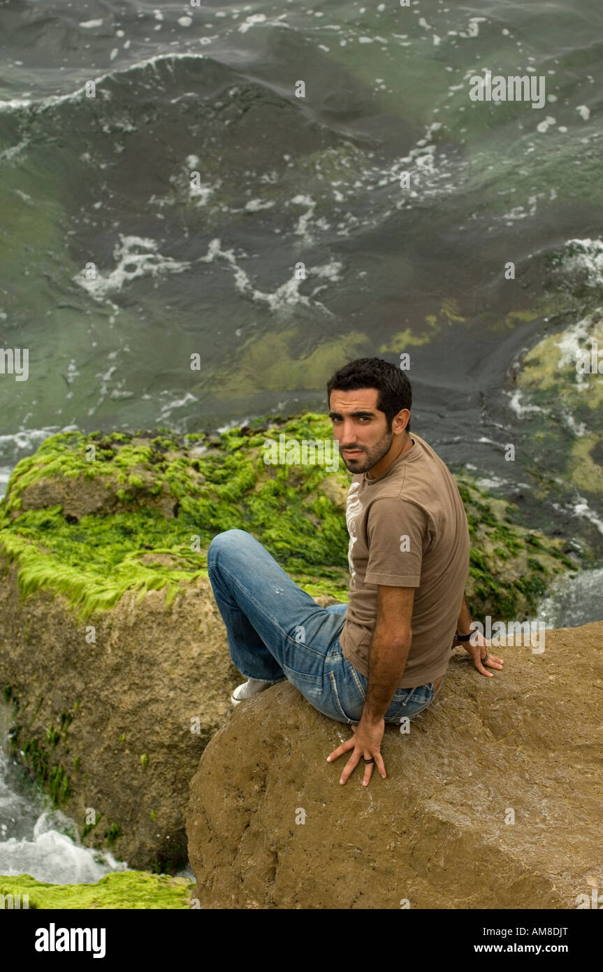young man sitting on rocks by the sea Stock Photo