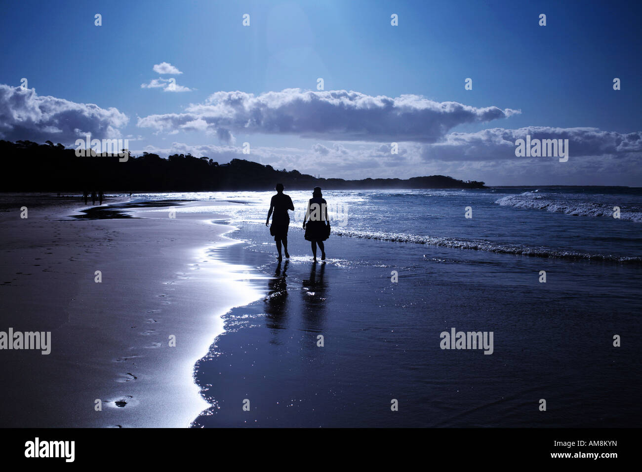 A couple walking along on a sandy beach in sunset Stock Photo - Alamy