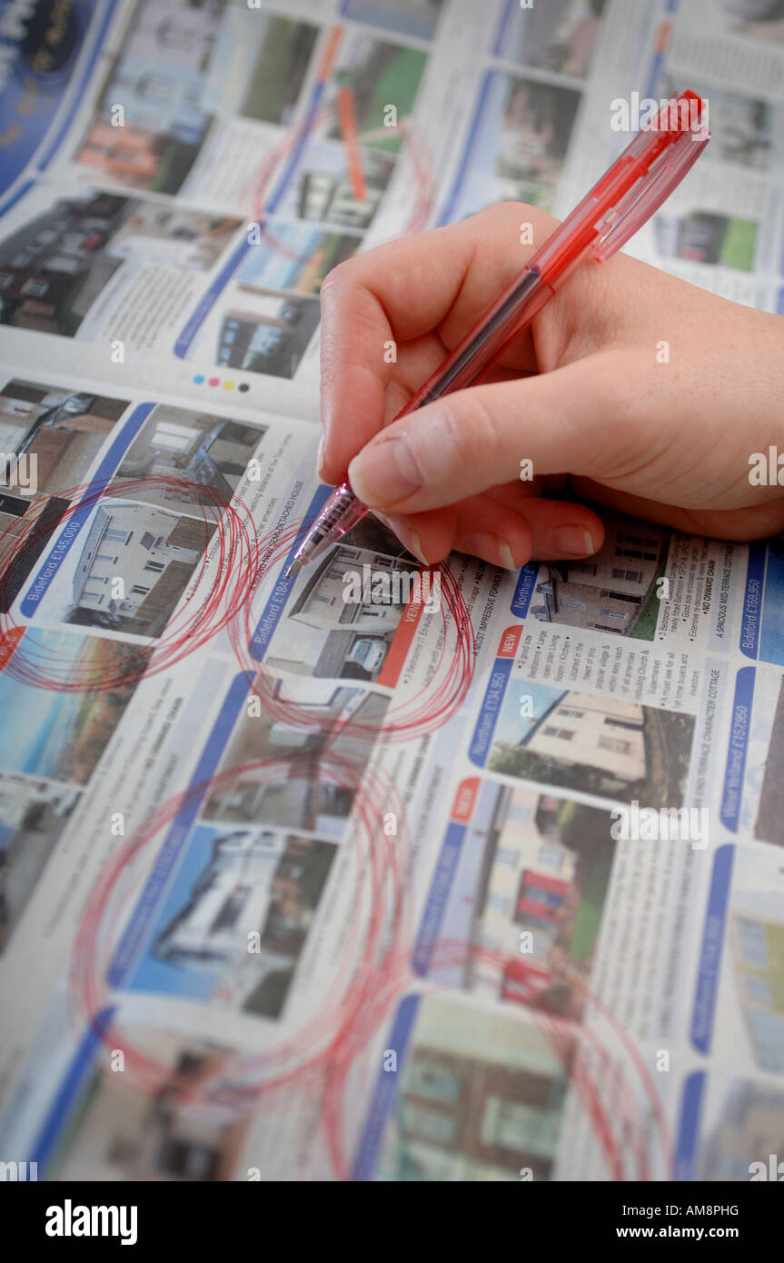 a hand holding a pen whilst searching for houses in the property section of a newspaper Stock Photo