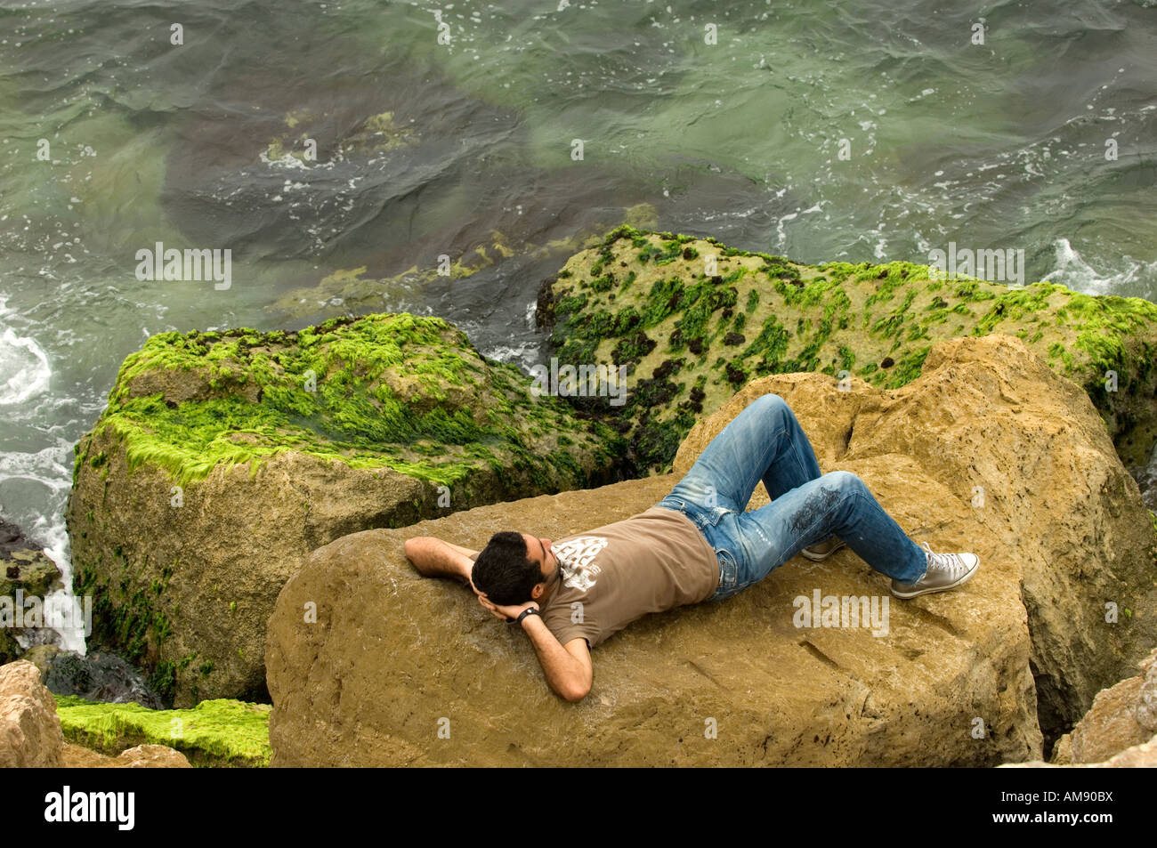 Man laying on rocks by the sea Stock Photo