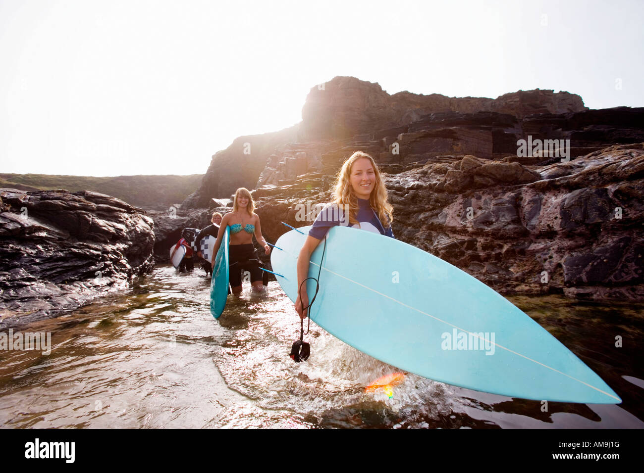 Four people carrying surfboards in the water smiling Stock Photo Alamy