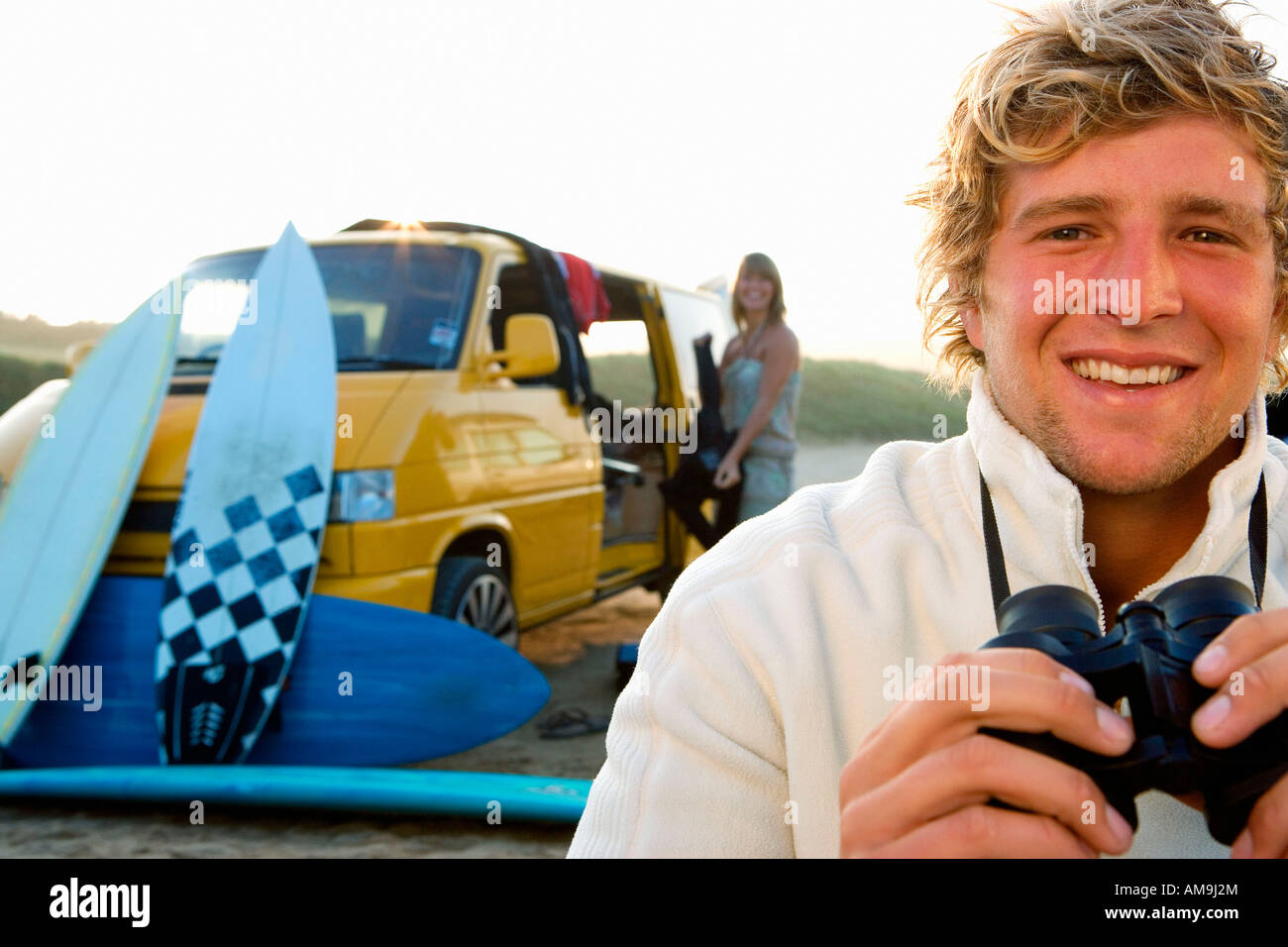 Man on beach with binoculars smiling with woman unloading van at the beach . Stock Photo