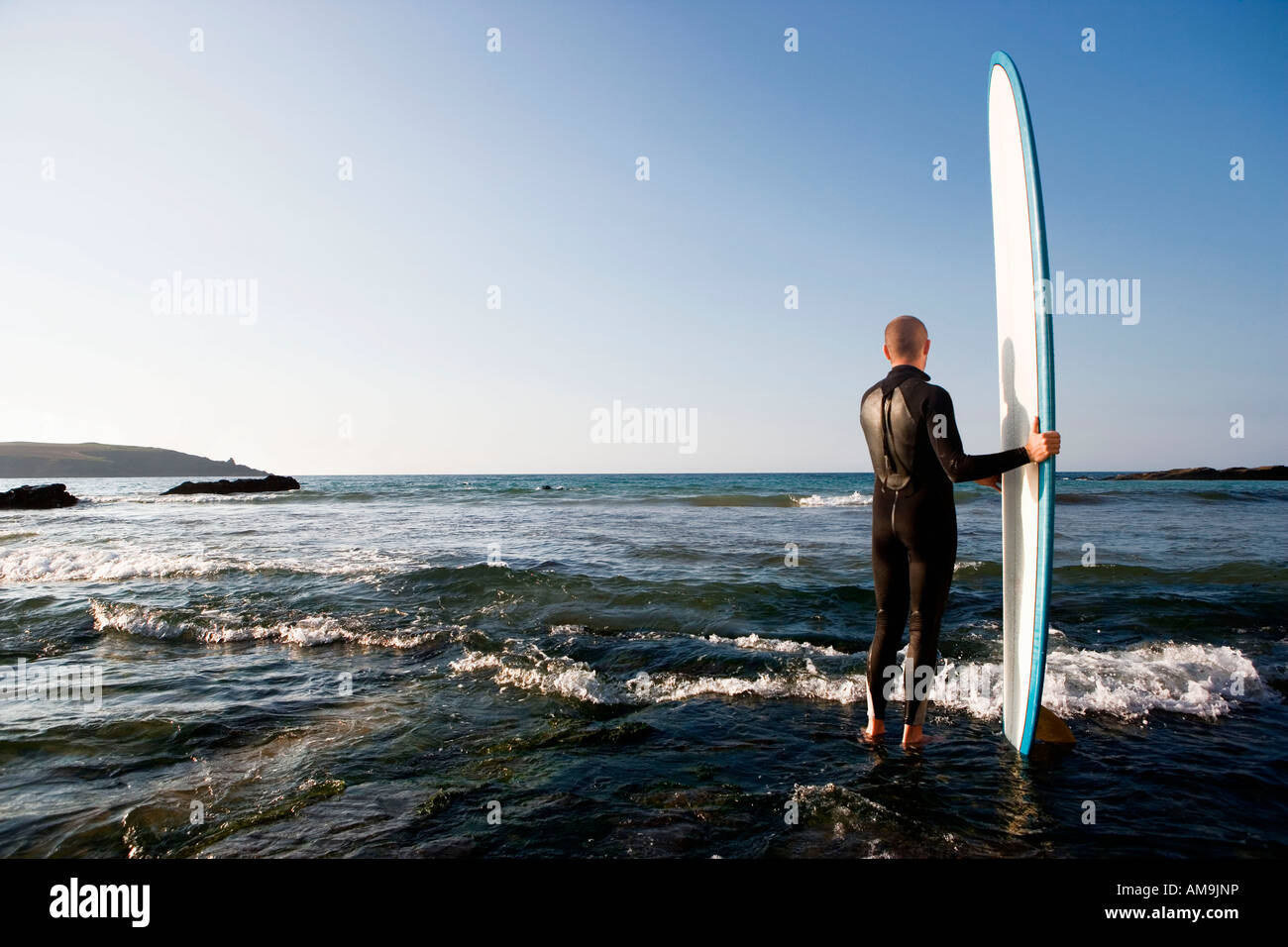 Man standing in shallow water with surfboard. Stock Photo