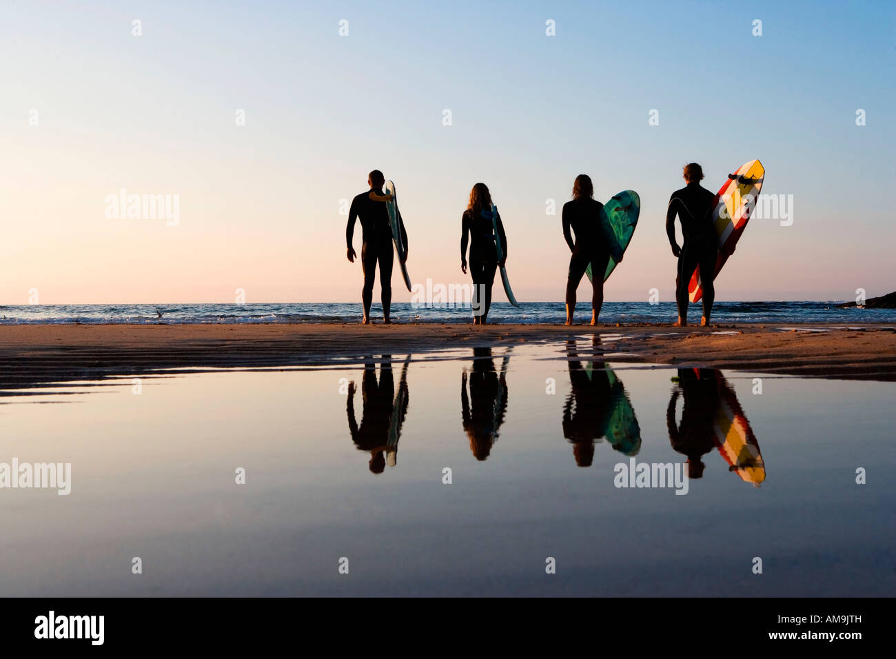 Four people standing on the beach with surfboards. Stock Photo