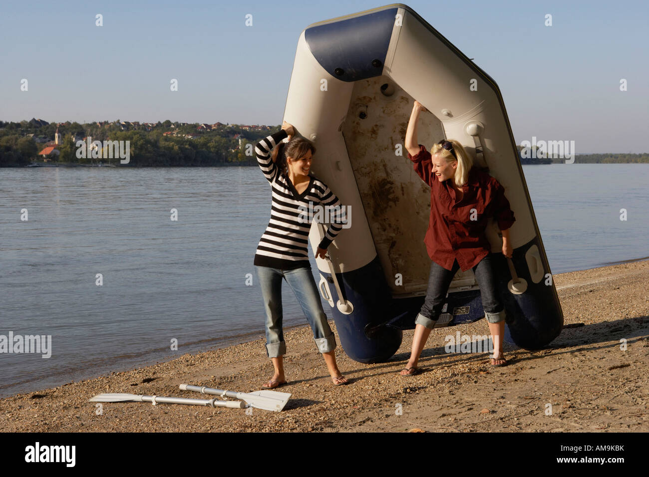 Two women carrying a raft on a beach smiling Stock Photo - Alamy