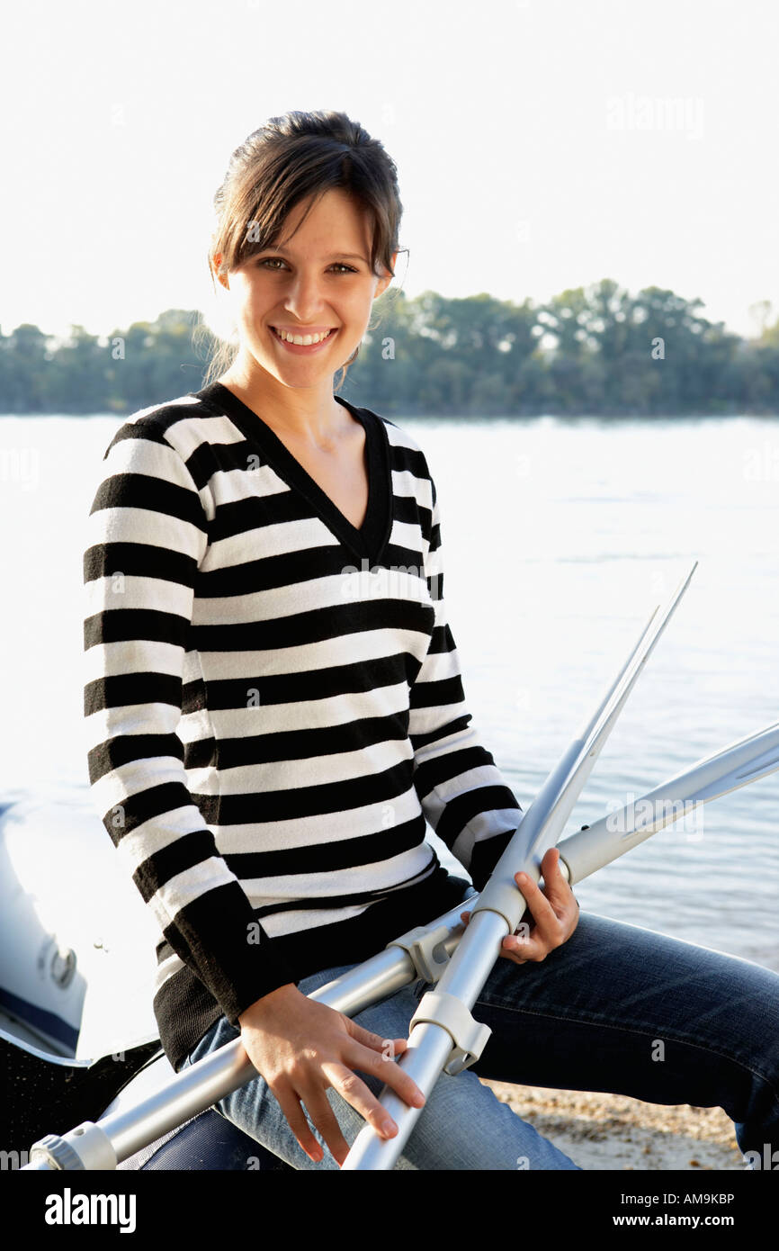 Woman leaning on a raft holding two oars smiling. Stock Photo