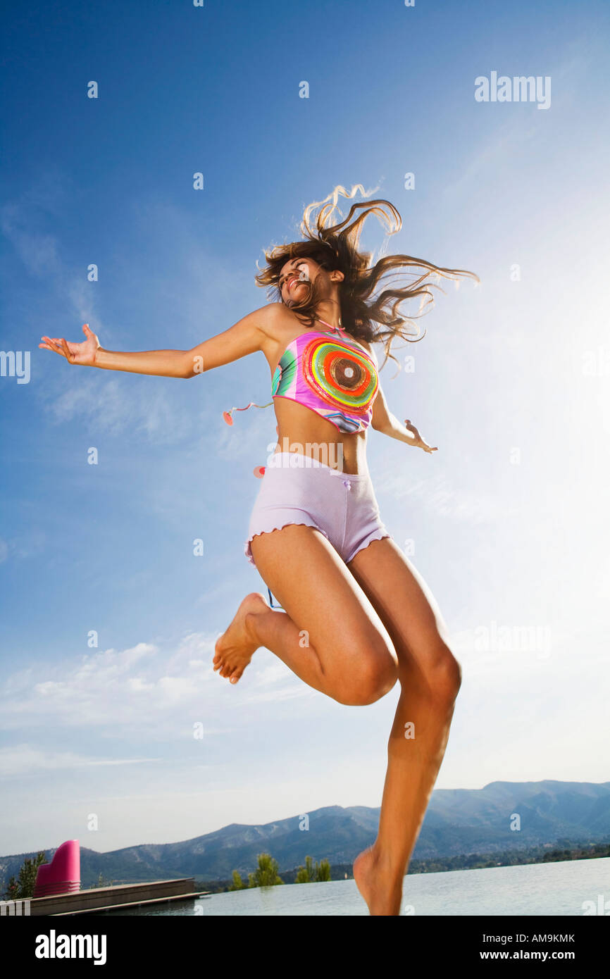 Woman jumps in air arms out wearing shorts outside. Stock Photo