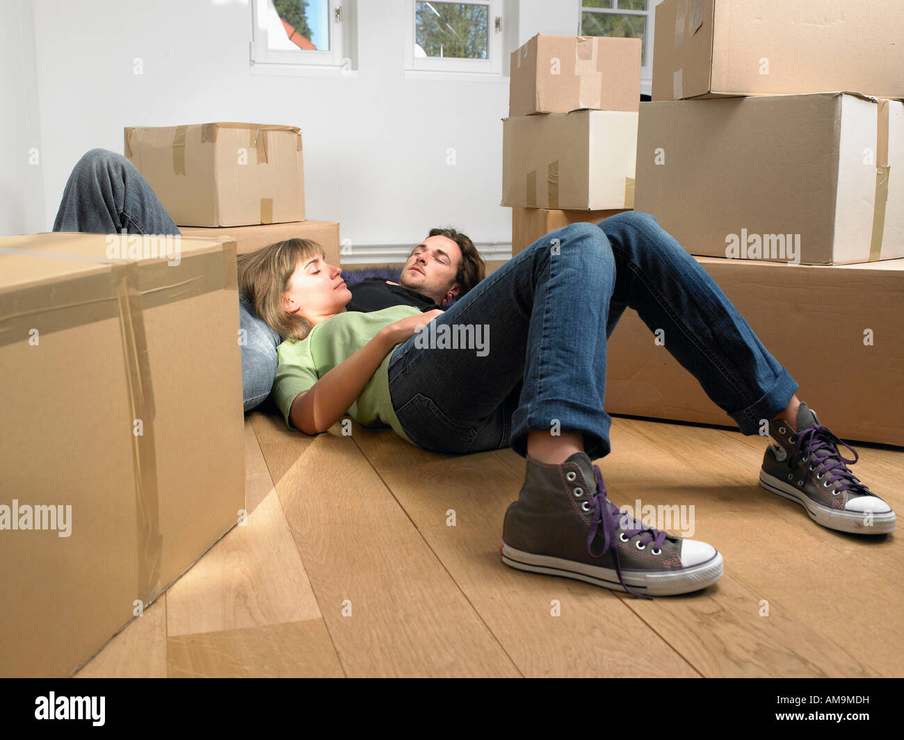 Couple sleeping on floor with moving boxes around them. Stock Photo