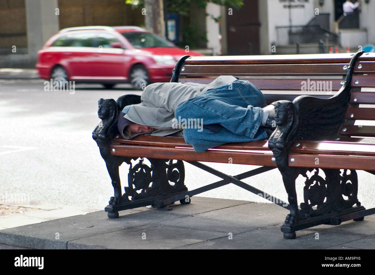 Homeless man sleeps on bench on Embankment London Stock Photo