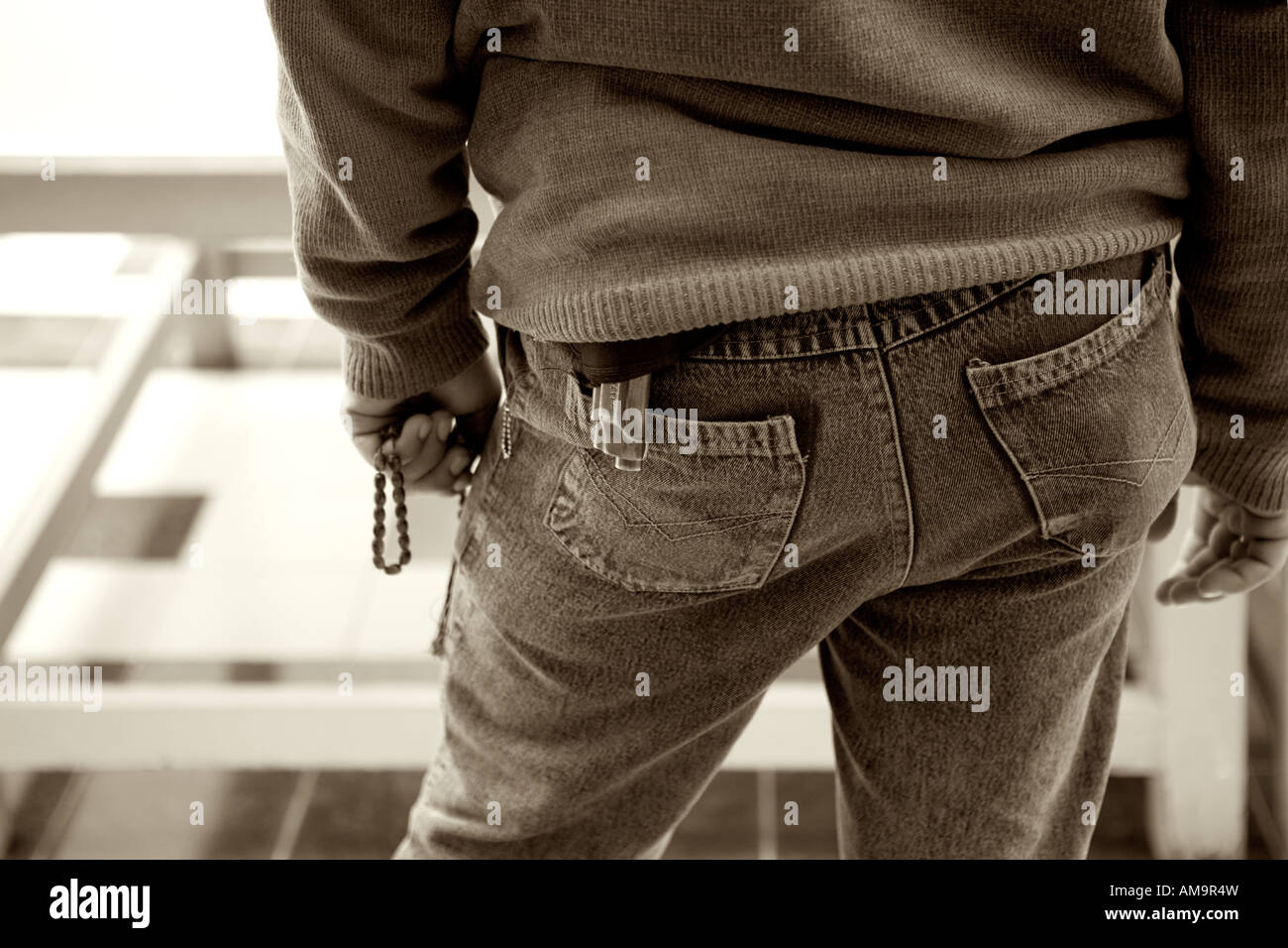 Back view of plain clothes policeman holding prayer beads with small pistol visible Stock Photo