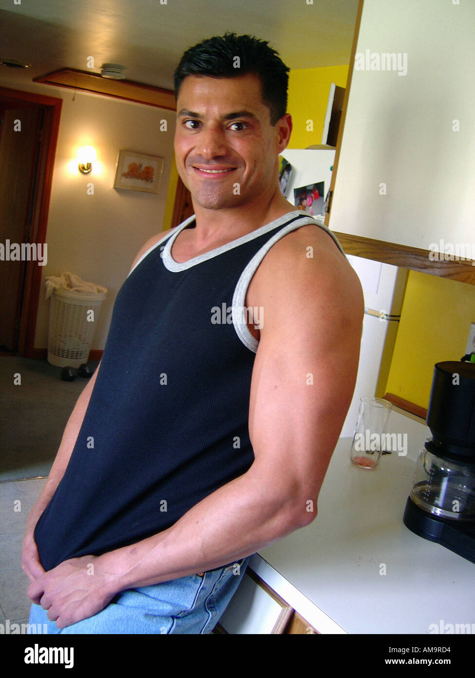 Casual Portrait of Man of Hispanic Ethnicity Wearing a Tank Top Standing in a Kitchen He is Wearing a Black Tank Top Singlet Stock Photo