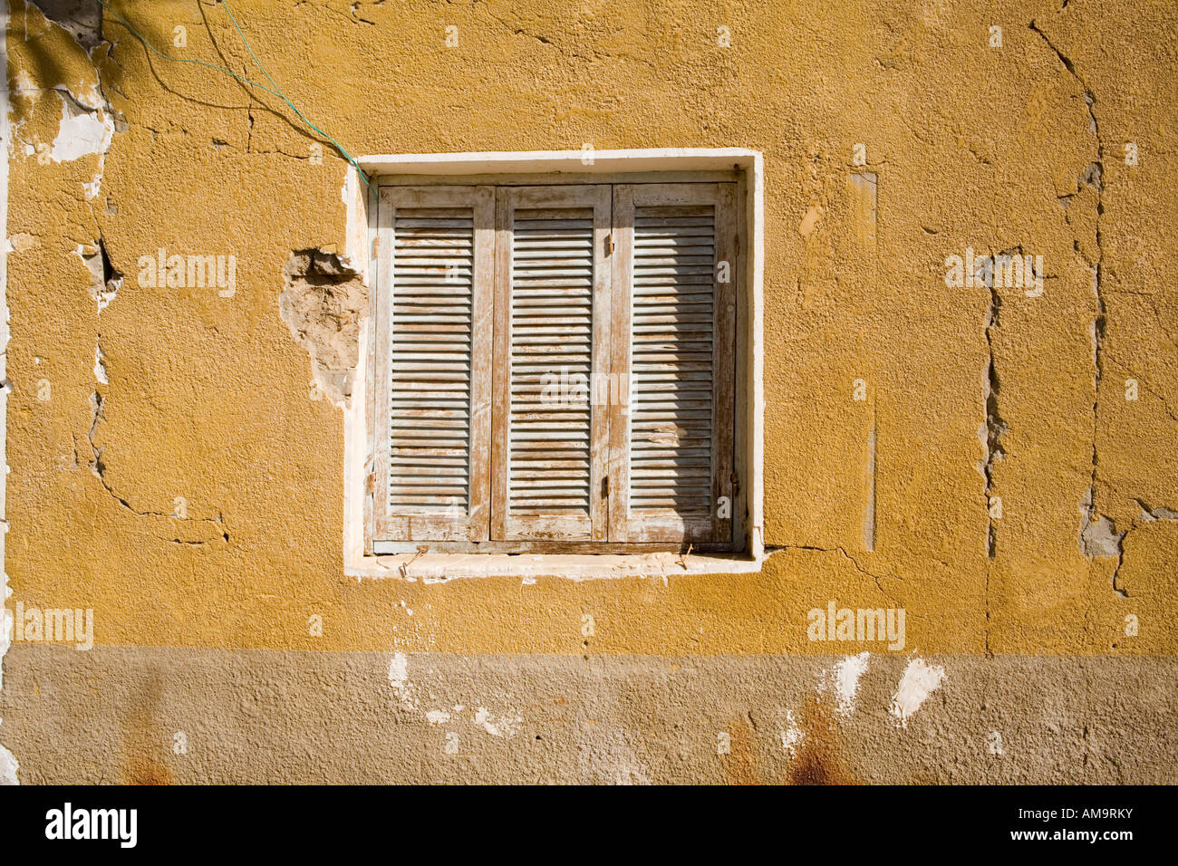 Old wooden framed window with shutters in painted mud brick wall in